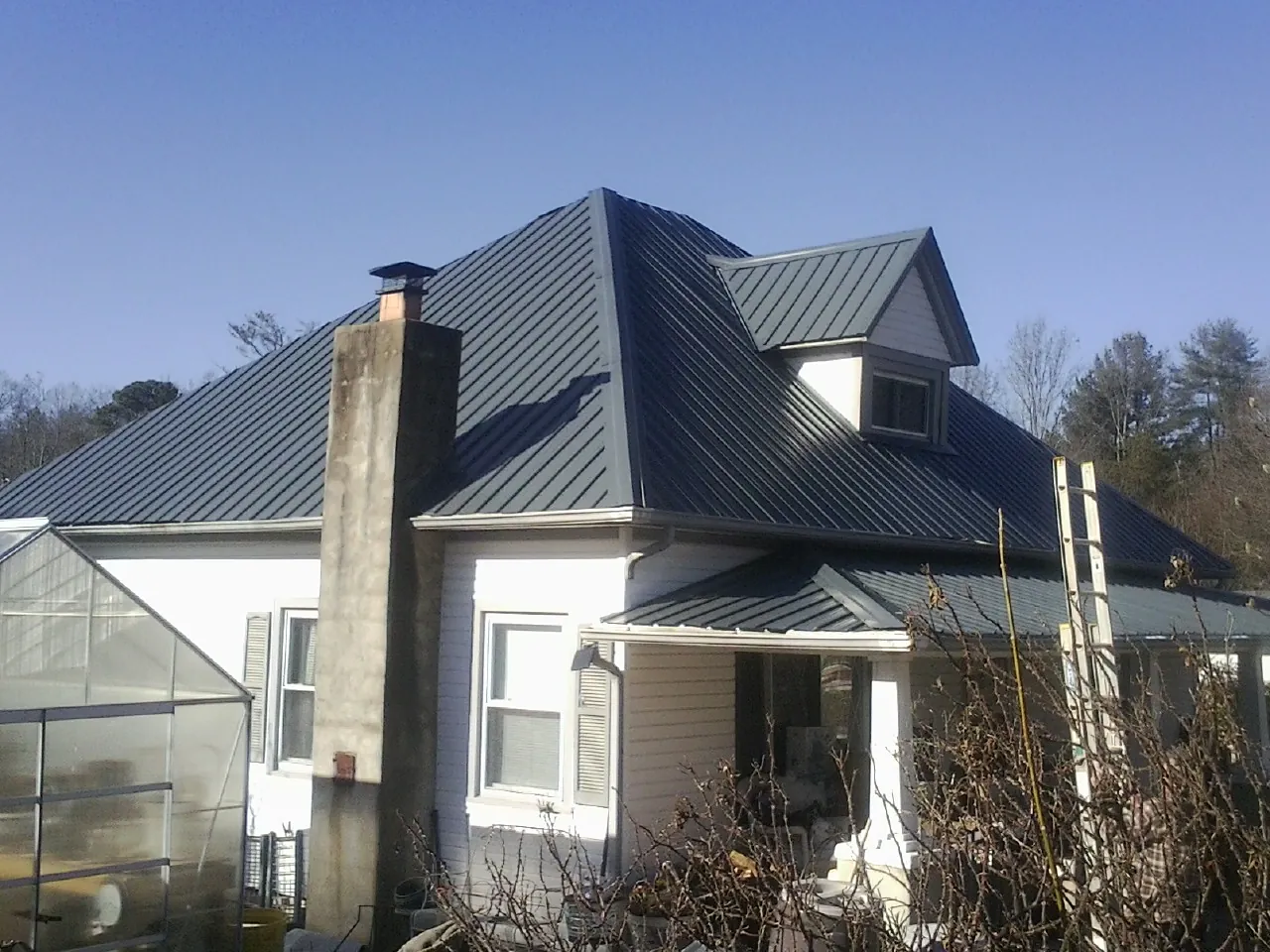 Dark blue standing seam metal roof on a white farmhouse with dormer — Slate & Tile Roof Repair by Roofing Brothers in Zionville