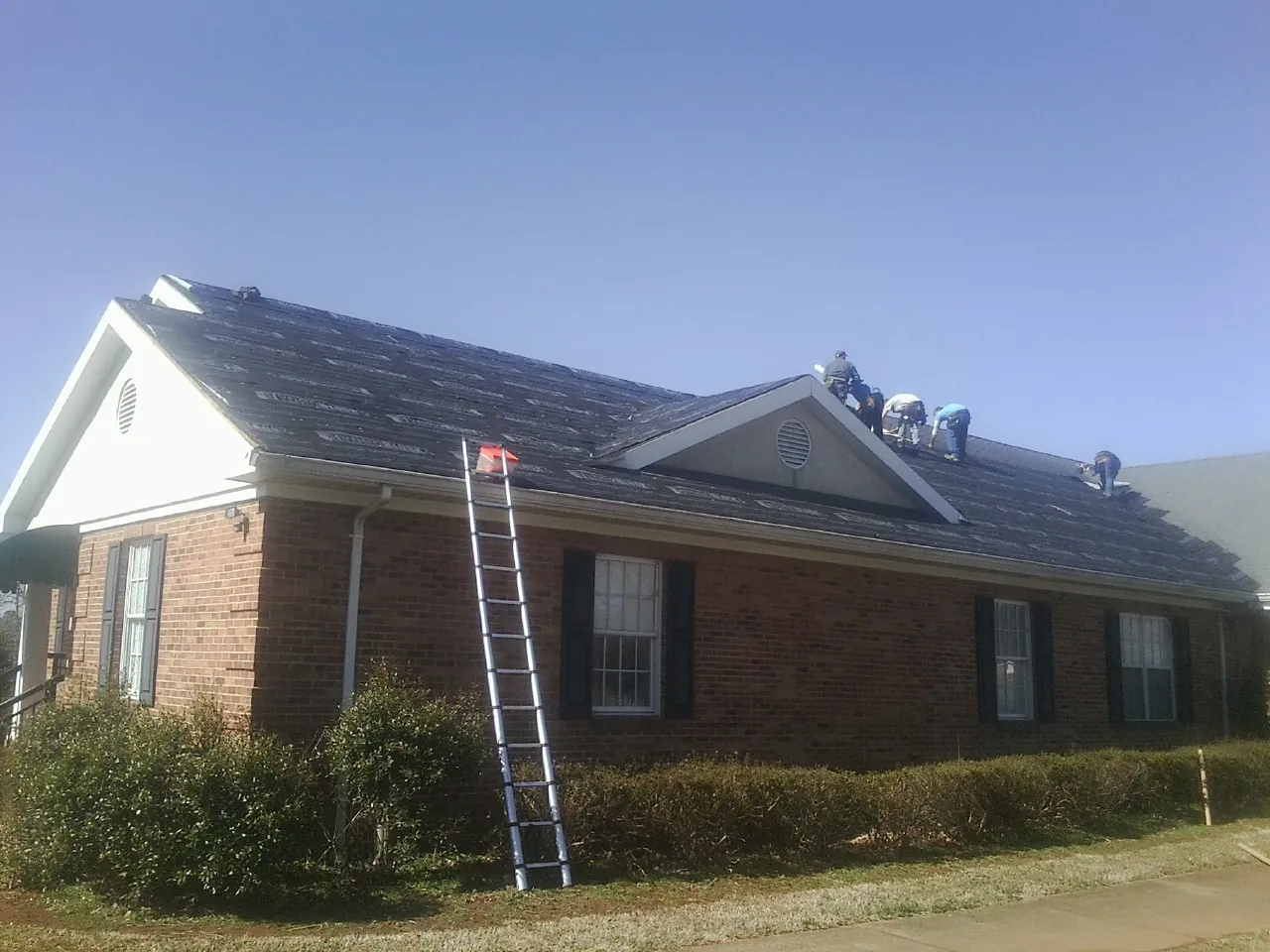 Crew tearing shingles off a brick ranch roof with a ladder set — Emergency Roof Repair work by our crew in Zionville