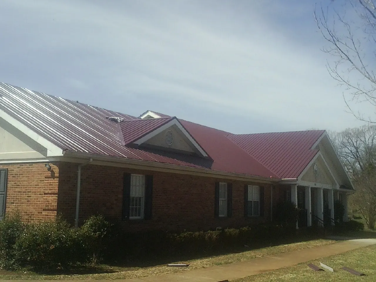 Red metal roof with gabled entries on a long brick building, from a Hail Damage Roof Repair job in Zionville