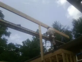 Carpenter setting a ridge beam over a new addition frame in Zionville