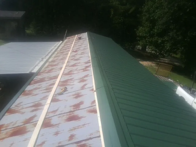 Old rusted panels beside newly installed green metal roofing — Wind Damage Roof Repair by Roofing Brothers in Zionville