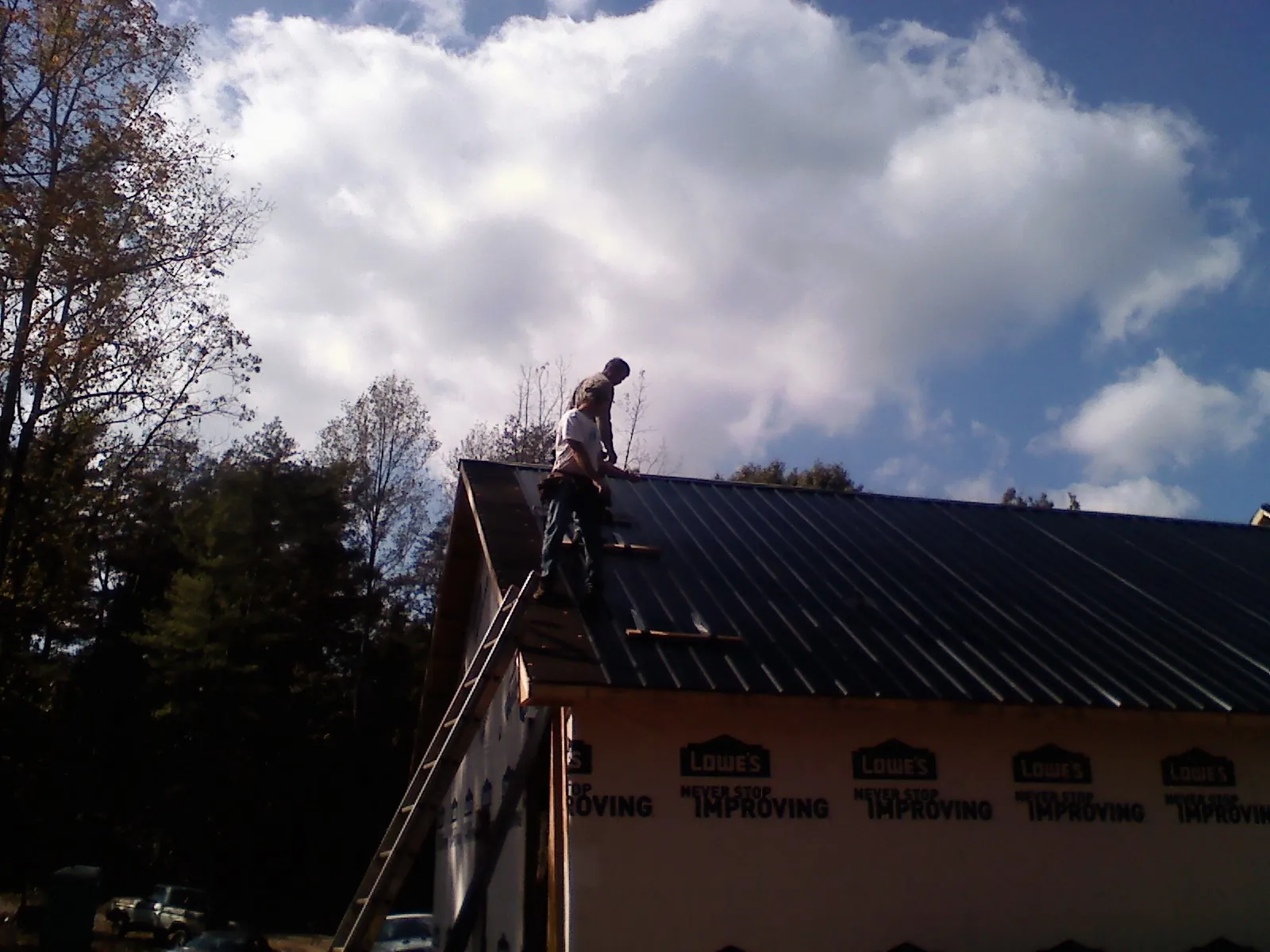 Roofer fastening dark metal panels high against a cloudy sky, from a Roof Inspection job in Zionville