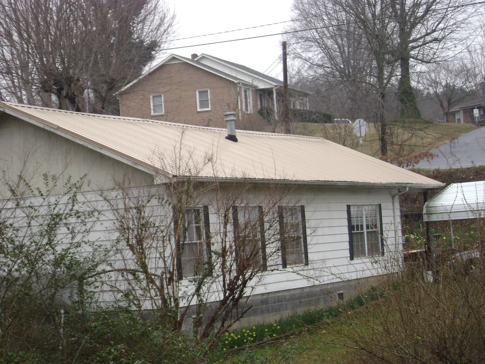 Tan metal roof on a white sided house set into a hillside — Commercial Roofing by Roofing Brothers in Zionville